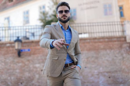 Foto de Fresco hombre de negocios elegante caminando con la mano en el bolsillo y posando con confianza de una manera de moda fuera - Imagen libre de derechos