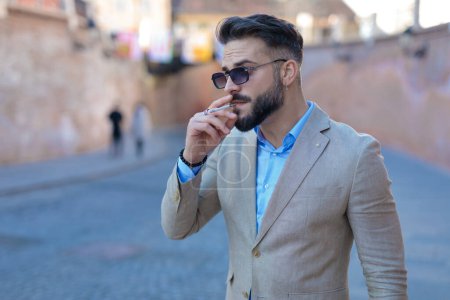Téléchargez les photos : Portrait of fashion elegant man smoking outdoor and looking to side in front of old city background - en image libre de droit