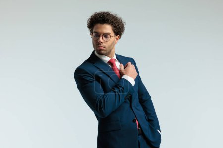 Foto de Retrato del atractivo hombre de negocios mirando hacia otro lado con un brazo hacia arriba, de pie y con gafas graduadas sobre fondo gris estudio - Imagen libre de derechos