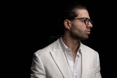 Téléchargez les photos : Homme sexy avec des lunettes portant chemise à col ouvert et regardant vers le côté tout en posant sur fond noir - en image libre de droit