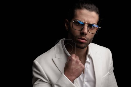 Téléchargez les photos : Portrait d'un bel homme élégant avec des lunettes ajustant chemise à col ouvert et posant devant fond noir - en image libre de droit
