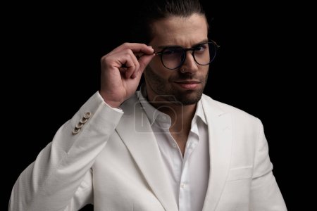 Téléchargez les photos : Sexy élégant homme en costume blanc souriant et des lunettes de réglage en face de fond noir - en image libre de droit