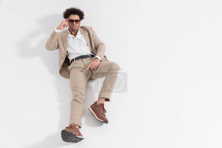 Foto de Sexy hombre con el pelo rizado acostado en el suelo y señalando el dedo a la sien en frente de fondo gris - Imagen libre de derechos