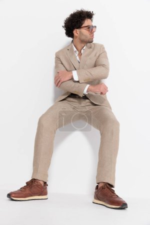 Photo for Handsome young man in smart casual outfit folding arms and looking to side while laying on the wall on grey background - Royalty Free Image