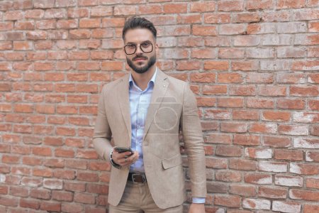 Photo for Portrait of young businessman posing while holding his phone and wearing eyeglasses outdoor, in an old medieval town - Royalty Free Image