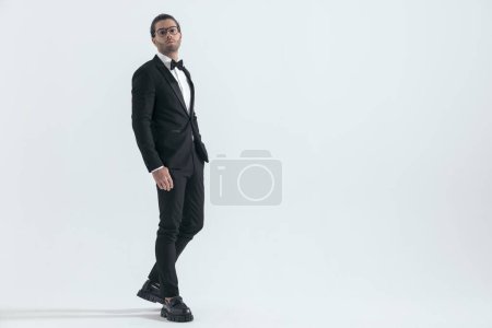 Photo for Side view of handsome young groom with hand in pockets walking and posing in front of grey background, full body - Royalty Free Image