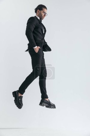 Photo for Sexy elegant businessman leaping up with hands in pockets and looking to side on grey background - Royalty Free Image