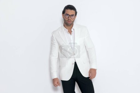 Téléchargez les photos : Sexy gars de la mode portant un costume veste blanche et chemise à col ouvert devant fond gris - en image libre de droit