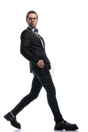 Téléchargez les photos : Homme d'affaires sexy marche large avec les mains dans les poches et portant des lunettes sur fond de studio blanc - en image libre de droit