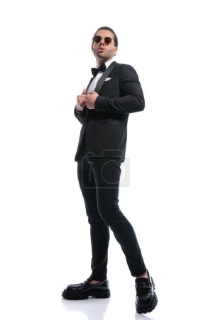 Photo for Young businessman arranging his tux with arrogance and wearing glasses against white studio background - Royalty Free Image