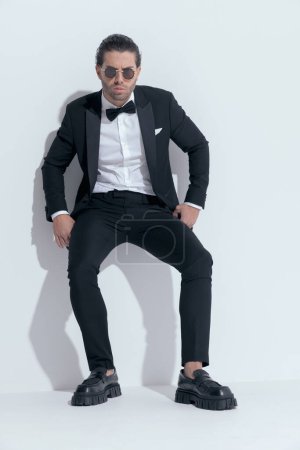 Foto de Sexy hombre de negocios apoyado en la pared con mirada loca, usando gafas contra fondo blanco estudio - Imagen libre de derechos