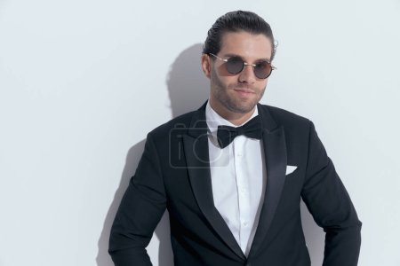 Foto de Elegante hombre de negocios dando una sonrisa sutil a la cámara, con gafas sobre fondo blanco estudio - Imagen libre de derechos