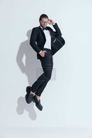 Foto de Sexy hombre de negocios saltando con las manos en los bolsillos y gafas de fijación, usando gafas contra fondo blanco estudio - Imagen libre de derechos