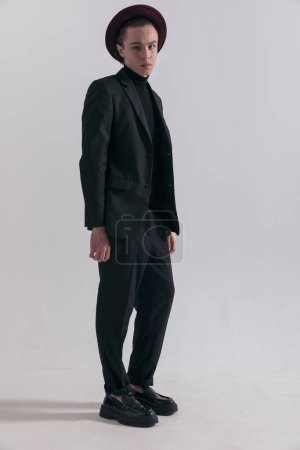 Foto de Imagen de moda de atractivo hombre de negocios de pie y posando con estilo y con un traje elegante contra fondo gris estudio - Imagen libre de derechos