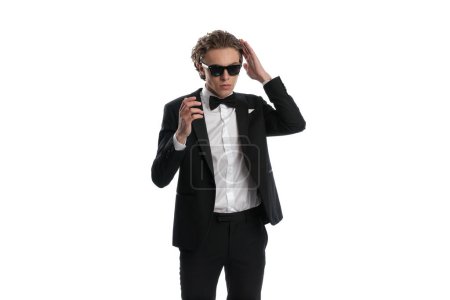 Téléchargez les photos : Jeune homme d'affaires arranger ses cheveux lisse dos, portant une tenue formelle sur fond de studio blanc - en image libre de droit