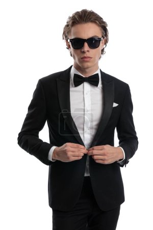 Photo for Handsome businessman opening his tuxedo with a badass vibe, wearing a formal outfit against white studio background - Royalty Free Image