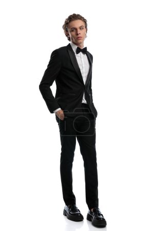 Photo for Young businessman walking with hands in pockets and looking away, wearing a formal outfit against white studio background - Royalty Free Image