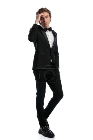 Photo for Sexy businessman folding one leg and touching forehead, wearing a formal outfit against white studio background - Royalty Free Image