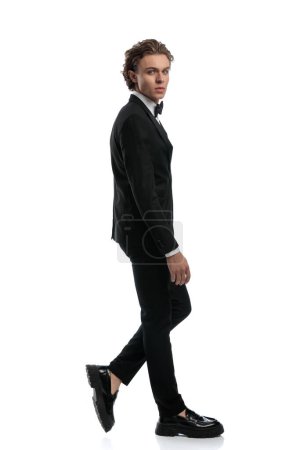 Photo for Handsome businessman walking and looking over the shoulder, wearing a formal outfit against white studio background - Royalty Free Image