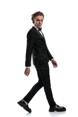 Foto de Elegante hombre de negocios caminando a un lado y mirando a la cámara, vistiendo un traje formal contra fondo de estudio blanco - Imagen libre de derechos