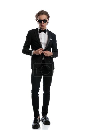 Photo for Young businessman with stylish look unbuttoning jacket, wearing a formal outfit against white studio background - Royalty Free Image