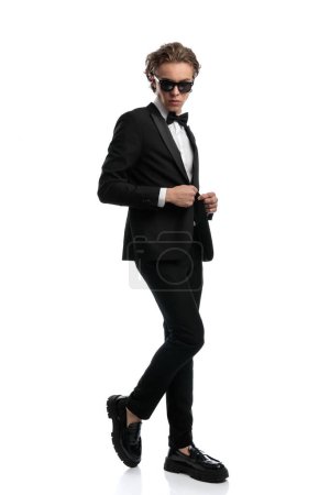 Téléchargez les photos : Bel homme d'affaires pliant une jambe et fermant sa veste, portant une tenue formelle sur fond de studio blanc - en image libre de droit