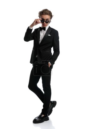 Photo for Sexy businessman looking over sunglasses with a relaxed stance, wearing a formal outfit against white studio background - Royalty Free Image