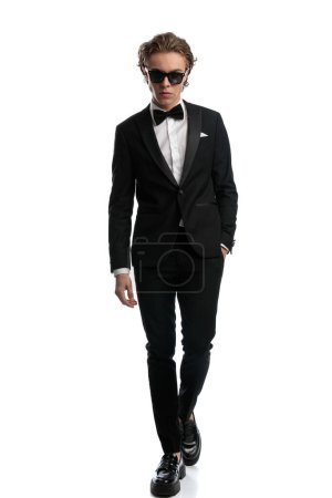 Photo for Attractive businessman putting one hand in pocket with badass walk, wearing a formal outfit against white studio background - Royalty Free Image