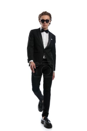Photo for Young businessman walking with a relaxed and cool style, wearing a formal outfit against white studio background - Royalty Free Image