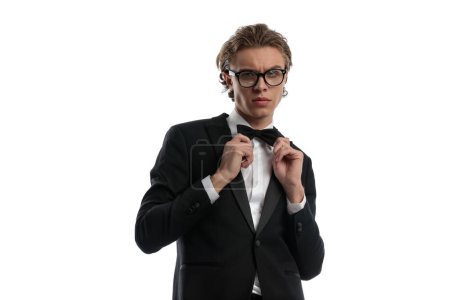 Photo for Handsome businessman fixing his bowtie and wearing eyeglasses, wearing a formal outfit against white studio background - Royalty Free Image