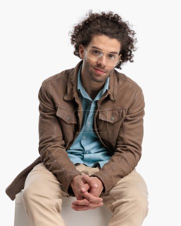 Téléchargez les photos : Portrait de type assis occasionnel en veste beige avec des lunettes assis devant fond blanc et souriant - en image libre de droit