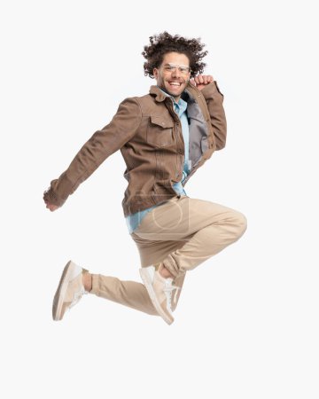 Téléchargez les photos : Vue latérale de l'homme décontracté dynamique riant et bondissant en l'air devant fond blanc en studio - en image libre de droit