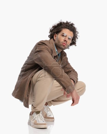 Photo for Side view of cool casual man with glasses and curly hair crouching in front of white background - Royalty Free Image