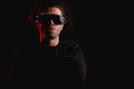 Téléchargez les photos : Cool fashion guy avec des lunettes croisant les bras et posant de manière confiante devant fond noir avec lumière rouge en studio - en image libre de droit