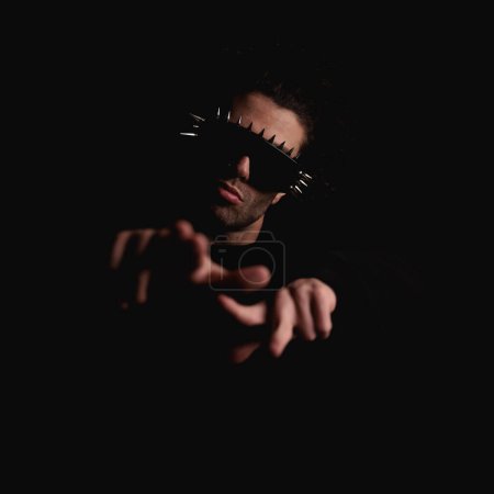 Photo for Sexy mysterious man with cool sunglasses making hand gesture and pointing fingers forward in front of black background - Royalty Free Image