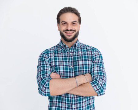 Téléchargez les photos : Portrait d'homme décontracté heureux en chemise à carreaux croisant les bras et souriant devant fond gris - en image libre de droit