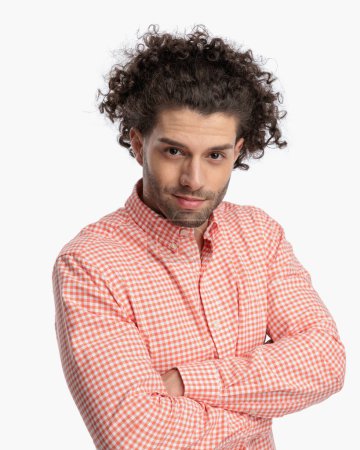 Téléchargez les photos : Portrait de jeune homme sexy aux cheveux bouclés en chemise à carreaux croisant les bras et souriant devant fond blanc en studio - en image libre de droit