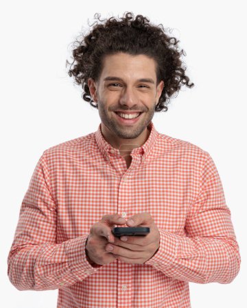 Photo for Happy casual man with curly hair laughing while texting messages in front of white background - Royalty Free Image