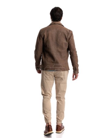 Foto de Vista trasera de hombre casual guapo en chaqueta marrón caminando delante de fondo blanco - Imagen libre de derechos