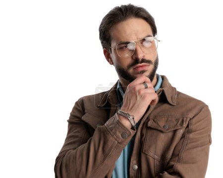 Téléchargez les photos : Homme réfléchi avec des lunettes toucher le menton et penser tout en regardant loin devant fond blanc - en image libre de droit