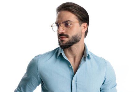 Foto de Retrato de hombre barbudo sexy con gafas mirando a un lado y posando delante de fondo blanco - Imagen libre de derechos