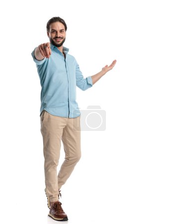 Photo for Full body picture of handsome casual man pointing finger forward while walking and inviting to side in front of white background - Royalty Free Image