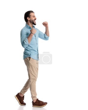 Photo for Side view of excited casual man holding fists up, yelling and celebrating victory in front of white background - Royalty Free Image