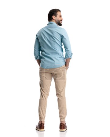 Photo for Back view of bearded casual man holding hands in pockets and looking to side in front of white background - Royalty Free Image