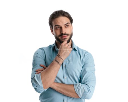 Foto de Hombre casual reflexivo en los brazos plegables camisa de mezclilla y pensar mientras se mira hacia otro lado en el fondo blanco - Imagen libre de derechos