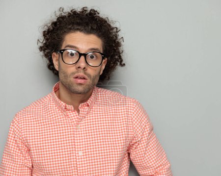 Photo for Portrait of handsome man with curly hair and glasses opening mouth and being surprised while posing in front of grey background in studio - Royalty Free Image