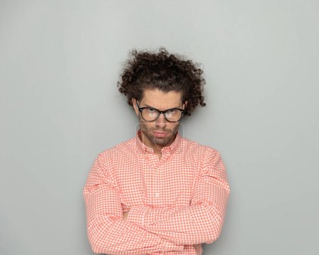 Photo for Portrait of upset young man with glasses crossing arms and frowning in front of grey background - Royalty Free Image