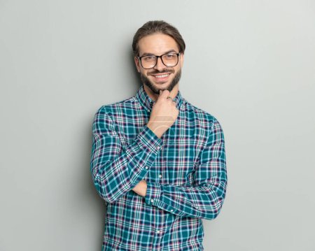 Foto de Confiado feliz hombre con gafas brazos cruzados, sonriendo y soñando mientras posando frente a fondo gris en el estudio - Imagen libre de derechos