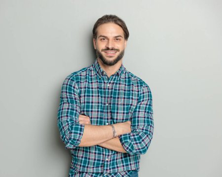 Foto de Retrato de hombre casual orgulloso en camisa a cuadros cruzando brazos y sonriendo delante de fondo gris - Imagen libre de derechos