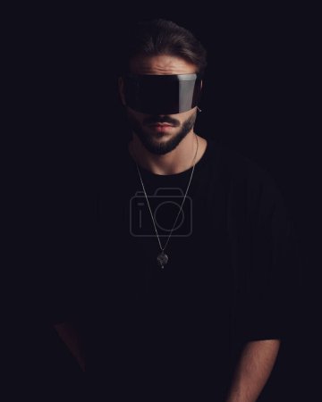 Foto de Joven sin afeitar con gafas mirando hacia adelante y posando frente al fondo negro - Imagen libre de derechos